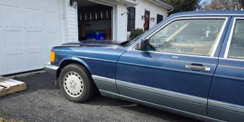 Navy Mercedes-Benz side profile in front of a white house and garage.