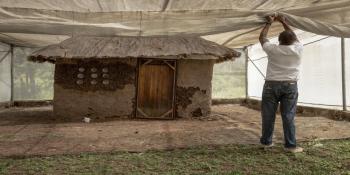 Man ties netting in front of a small house.