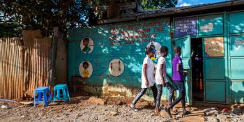 Three young kids walk to a blue-colored shelter.