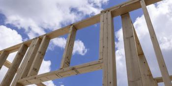 Low angle photo of wooden house framing with blue sky behind it.