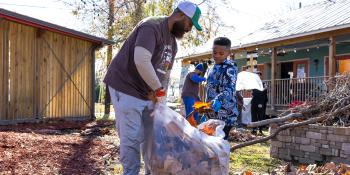 A man works with a young child to rake leaves into a bag at their neighborhood clean-up.