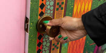 A hand with green painted nails pulls open a door with an illustrated image on it. The frame of the door is pink.