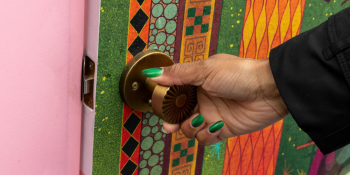 A hand with green painted nails pulls open a door with an illustrated image on it. The frame of the door is pink.