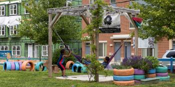 Two kids play in a colorful hammock in a park.