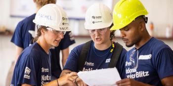 Three student volunteers wearing Habitat shirts and hard hats look at a paper.