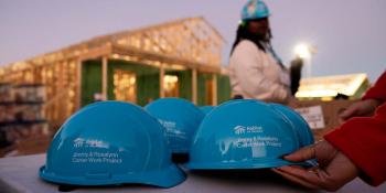 Habitat hard hats sit on a table in the foreground with a hand reaching out for one.