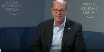 Jonathan Reckford moderates a panel at WEF26. He is seated in front of a backdrop with WEF logos.