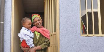 Woman standing in doorway of house holding her child. 