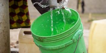 A woman fills up a green bucket with water from a kiosk.