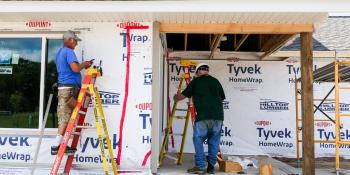 Two men work on a construction site of an unfinished house.