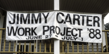 A large white banner hangs on the front porch of a home. The black text says "Jimmy Carter Work Project '88 June 27-July 1"