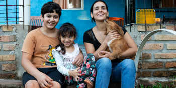 Woman, two kids and dog posing happily in front of their home.