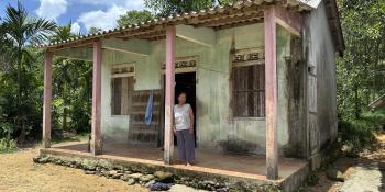 Woman standing on porch of white house with pink posts.