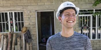 Young man wearting white hard hat and smiling in front of a concrete block home