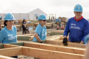 Jonathan Reckford and two volunteers carry wooden house framing on the site of the 2025 Carter Work Project.