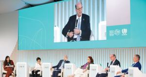Six speakers on stage at WUF13. Second from the right is Habitat CEO Jonathan Reckford, who can also be seen on a large screen above the stage speaking into a microphone. 