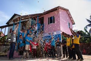 Un grupo de voluntarios celebra frente a una casa rosa de Habitat recién construida lanzando confeti al aire.