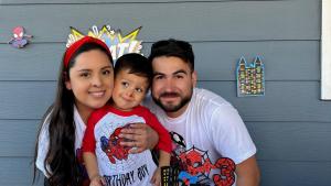Mother, son and father posing in front of spiderman birthday decorations.