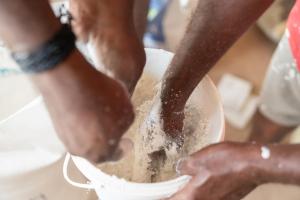 Multiple hands reach into a bucket to help mix a building material.