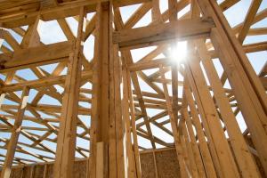 Sun shining through roof trusses of wood house frame.