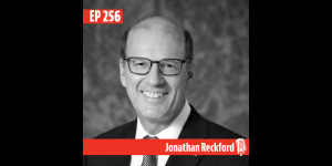 Black and white headshot of Jonathan Reckford with red and white graphic elements. The top left graphic says "EP 256" and the bar across the bottom of the photo says "Jonathan Reckford" followed by an illustration of an old-fashioned microphone. 