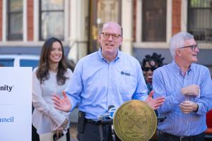 Habitat CEO Jonathan Reckford speaking at a lectern displaying the seal of the city of New York. Several other speakers at the ceremony stand behind him.
