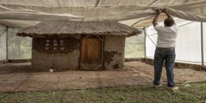 Man ties netting in front of a small house.