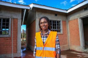 A woman wearing a construction vest stands before a construction site