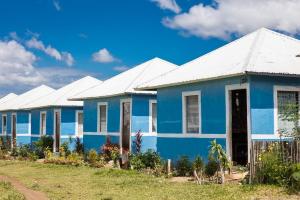 Row of bright blue Habitat houses with white roofs in front of a clear blue sky with fluffy white clouds.