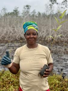 A woman holds a mangrove seedling and a thumbs up