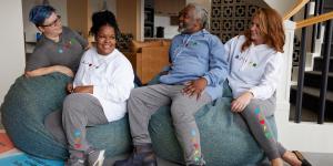 A group of four people smiling and laughing as they lounge on big bean bag chairs, swearing Habitat sweatshirts and sweatpants.