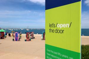 A branded column that says let's open the door in the forefront. In the background is a pop-up door installation displayed in front of a lake.