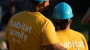 A pair of homeowners in yellow shirts that read, "habitat family," hugging during sunrise.