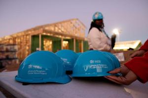 Habitat hard hats sit on a table in the foreground with a hand reaching out for one.