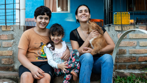 Woman, two kids and dog posing happily in front of their home.