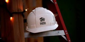 A ladder with white string lights wrapped around it and a white hardhat with Habitat logo sitting on one of the steps. 