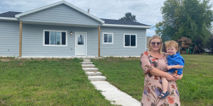 Woman holds her 2-year-old son in front of their Habitat home.