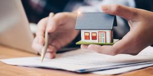 Hands holding a small model home and signing papers