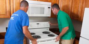 Two men fitting a new Whirlpool oven unit into a kitchen
