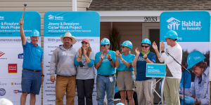 Twin Cities Habitat representitive holds a hammer up while on stage at Carter Work Project 2023