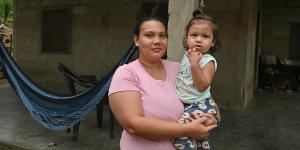 Mujer sostiene en brazos a una niña pequeña frente a su vivienda, que cuenta con piso de concreto y un entorno más seguro y adecuado para la vida cotidiana. La imagen refleja el impacto de una mejora habitacional en el bienestar de las familias. 