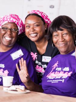 Three women in purple shirts smiling.