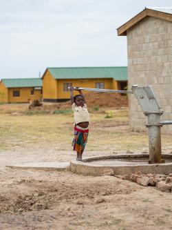 Child pulling on lever on a community water pump.