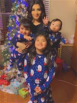 Mother with three kids in matching holiday pajamas in front of their Christmas tree