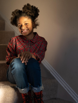 Young Black girl smiling while sitting on carpeted stairs in her Habitat home.