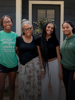 Three teenage girls and their grandmother pose happily together in front of their home.