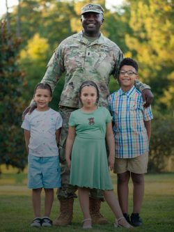 A man in a military uniform poses with his arms around his young daughter and two young sons.