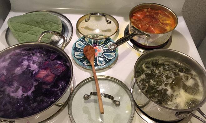 Pots of water boiling on a stove with various colored ingredients in them.