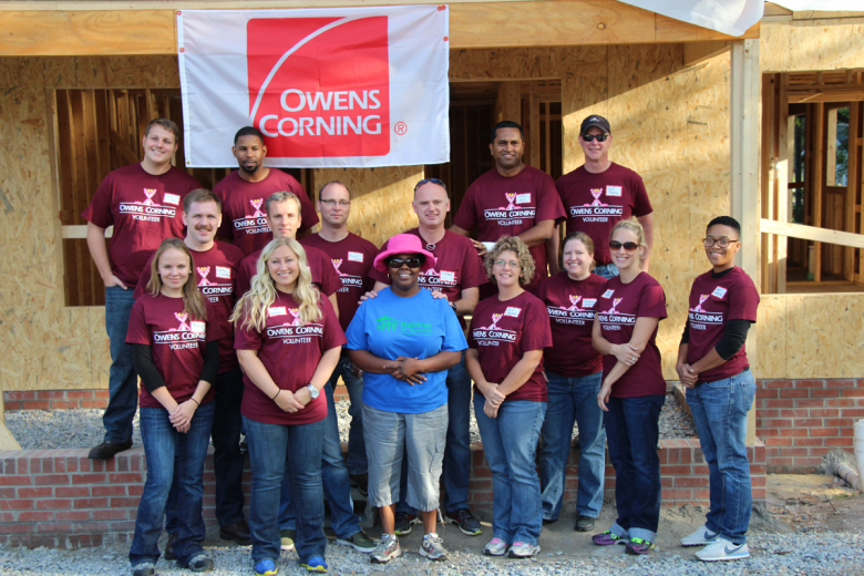 Group of Owens Corning volunteers stand with homeowner on a build site.
