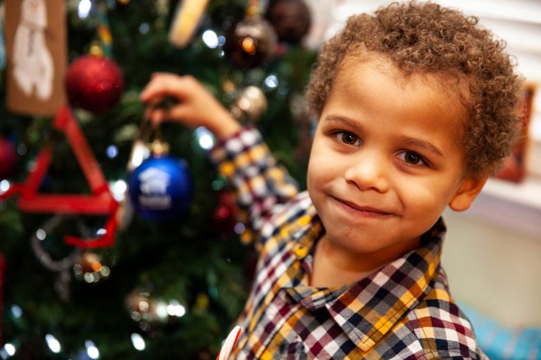 Little boy hangs ornament on Christmas tree.